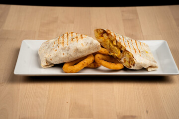 Grilled wrap filled with chicken and vegetables served with onion rings on a white plate