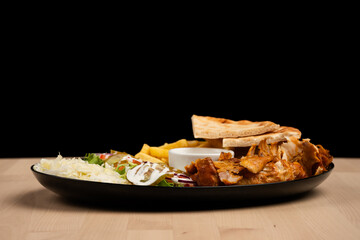 Delicious plate of mixed salad, fries, pita bread, chicken and sauce on a wooden table