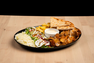 Delicious plate of mixed doner kebab with salad, fries, pita bread, and sauce on a wooden table