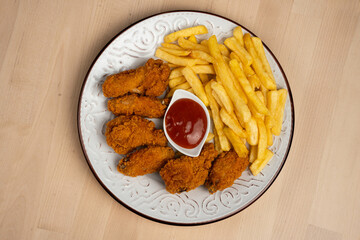 plate of crispy fried chicken wings with French fries and a side of ketchup on a wooden table