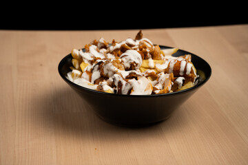 Bowl of loaded fries topped with creamy sauce and grilled chicken on a wooden table