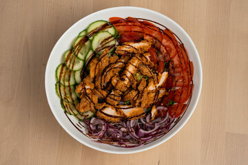 fresh salad bowl with crispy chicken, cucumbers, tomatoes, and red onions on wooden table