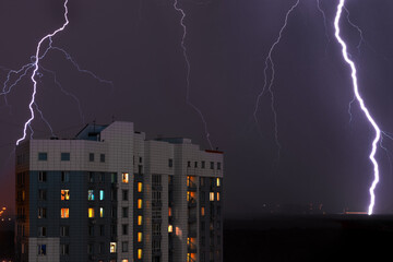 Thunderstorm with lightning bolt strikes and storm over city in purple light at night building with...