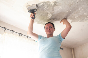 a woman using a spatula removes the top layer of old paint on the ceiling