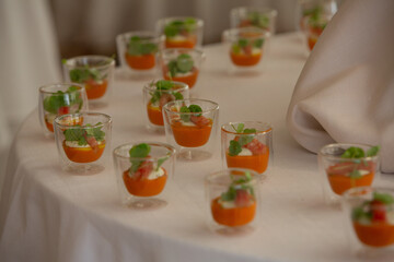Rows of verrines with bright orange appetizers are standing on the white tablecloth
