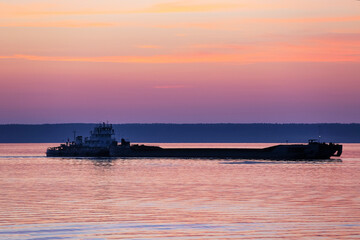 A barge floats on the river at sunset