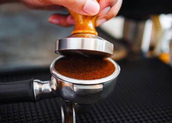 Close-up of hand Barista cafe making coffee with manual presses ground coffee using tamper at the coffee shop