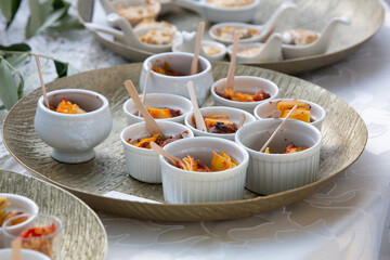 Small white bowls with appetizers are standing on a golden tray