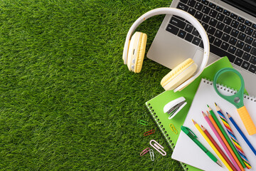 Colorful school supplies arranged with a laptop and headphones on a grass surface, perfect for back...