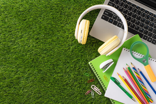 Colorful school supplies arranged with a laptop and headphones on a grass surface, perfect for back to school concepts