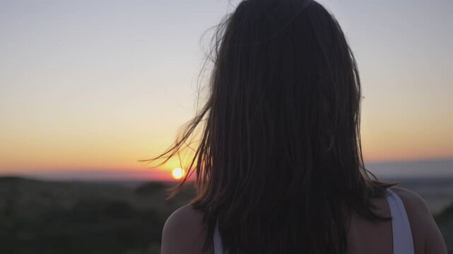 Slow motion. Gorgeous young woman looking at a magnificent summer sunset. View from the back. The camera moves