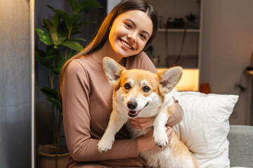 Happy young girl, teenager embracing her pembroke welsh corgi dog at home