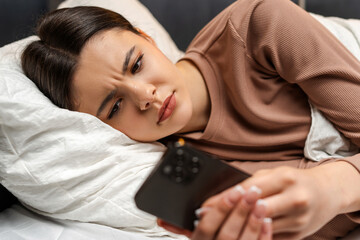 Young girl, teenager feeling frustrated while using smartphone in bed