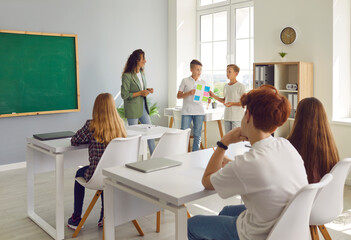 Obraz premium In a classroom setting, two students with teacher, presenting and explaining homework during lesson. Collaborative atmosphere, enhancing the learning experience within the school environment.