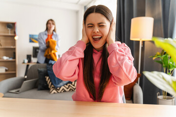Young girl, teenager covering ears with hands while roommate is making noise