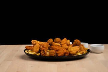 Plate of crispy fried chicken and fries on a wooden table with a black background