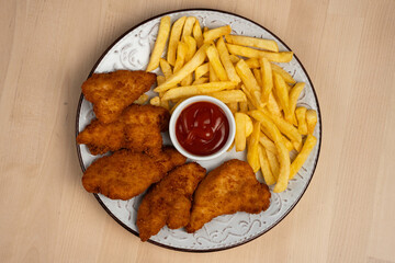 Top view of plate of crispy fried chicken wings with french fries and a ketchup on a wooden table
