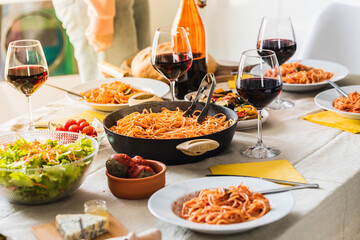 Family preparing table enjoying traditional italian spaghetti dinner with red wine and salad