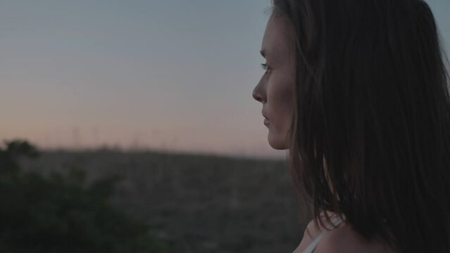 Slow motion. Gorgeous young woman looking at a magnificent summer sunset. Portrait. The camera moves