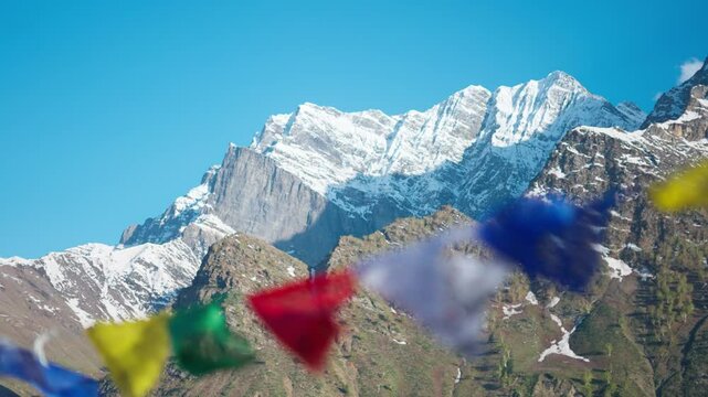 4K Rack focus shot of Buddhist prayer flags waving in the wind in front of the Snowy Himalayas as seen from Khangsar Village in Lahaul, Himachal Pradesh, India. Focus from Prayer flag to the mountain.