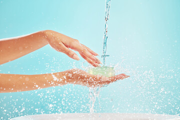 Water, cleaning and person hands with soap, washing and hygiene in studio for wellness. Health, care and morning routine with splash, protection and safety from germs with blue background in bathroom