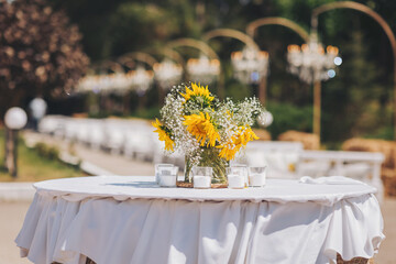 Beautiful sunflower and baby's breath centerpieces at wedding reception and blurred chandeliers on background. Luxurious crystal chandeliers in the middle of a forest.Wedding decoration with sunflower
