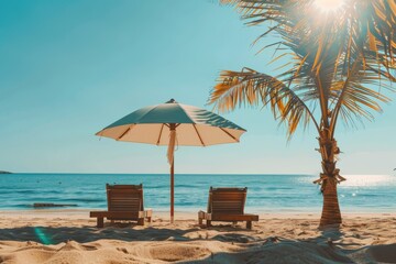 Naklejka premium Two lounge chairs positioned under a single umbrella with a palm tree beside them, facing the calm blue ocean on a golden sunny beach, perfect for a peaceful escape.