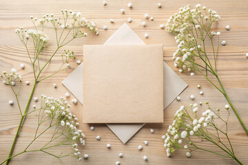 Elegant square invitation card mockup adorned with delicate gypsophila flowers on a rustic beige table, perfect for wedding or baby shower stationery designs.
