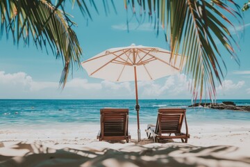 A peaceful beach setting showcasing two wooden lounge chairs under a white umbrella, with vibrant palm leaves framing the view of the ocean's clear blue waters.