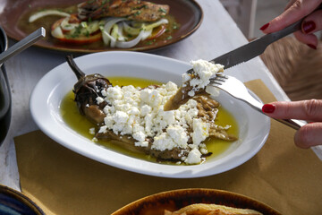 Woman is eating roasted eggplant stuffed with feta cheese in olive oil, Mediterranean summer lifestyle