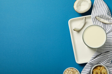 Glass of milk, towel, coconut and sliced bananas on blue background, space for text