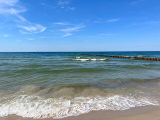 Coastal landscape with soft waves and a wooden breakwater against a cloudless sky