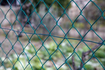 Fototapeta premium Close-up of a green wire mesh fence with a blurred garden in the background