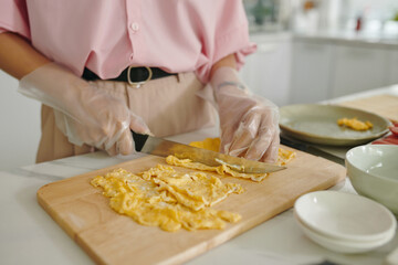 Close-up of housewife in gloves cutting egg pancake for cooking special dish