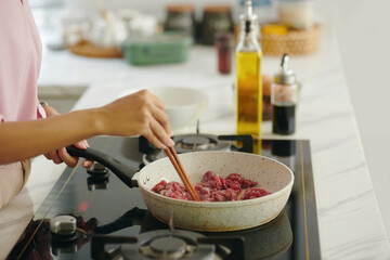 Close-up of woman frying meat on stove for dinner in the kitchen
