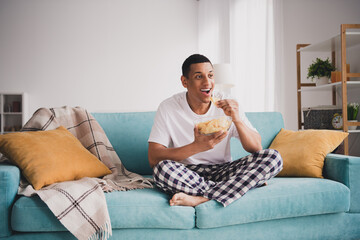 Photo of cheerful positive guy sleepwear pajama staying home sofa watch soccer eating chips indoors...
