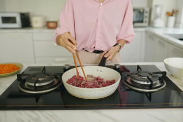 Close-up of housewife frying meat on pan for dinner in the kitchen at home