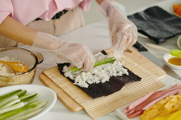 Close-up of woman in gloves making korean kimbap in the kitchen
