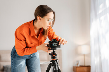 Positive happy woman adjusting camera on tripod, smiling, preparing for online conference