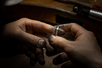 Closeup of a diamond wedding ring and dirty jeweller hands holding it