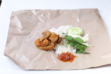 Pecel ayam or ayam penyet is a traditional Javanese food from Indonesia served with fried chicken, rice, cucumber, cabbage, basil and chili sauce isolated on white background, on paper packaging