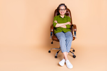 Full size photo of pretty senior female crossed hands sit armchair wear trendy green outfit isolated on beige color background