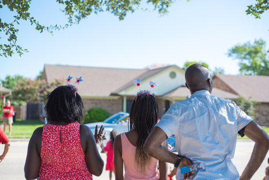 Unidentified African American families with hair hoop decoration waving hands watching Independence Day parade on residential street, July Fourth freedom celebration in Coppell, Texas, patriotism