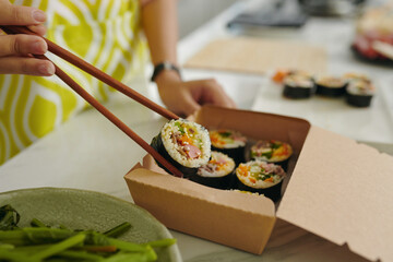Close-up of woman using sticks to pack ready kimbap in carton box