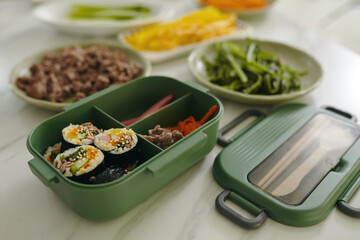 Close-up of lunchbox with korean kimbap and vegetables on kitchen table