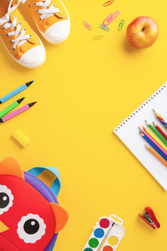 A vertical flat lay of colorful back to school supplies including shoes, backpack, pencils, and an apple on a yellow background
