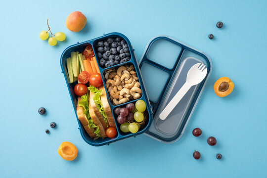 Top view of a colorful and balanced school lunch with fresh fruits, vegetables, sandwich, and nuts in a blue lunch box