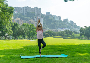 A cute little girl doing yoga on the park grass
