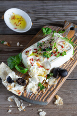 A piece of fresh feta cheese (paneer) with olives, herbs, spices and slices of flatbread (tortilla, lavash, pitta, chapatti) on a wooden board and a dark background. Greek cuisine dish, healthy food.