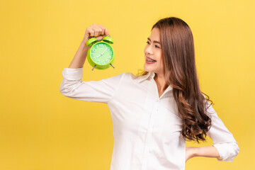 Smiling young woman with braces on her teeth with long brown hair standing holding green alarm...